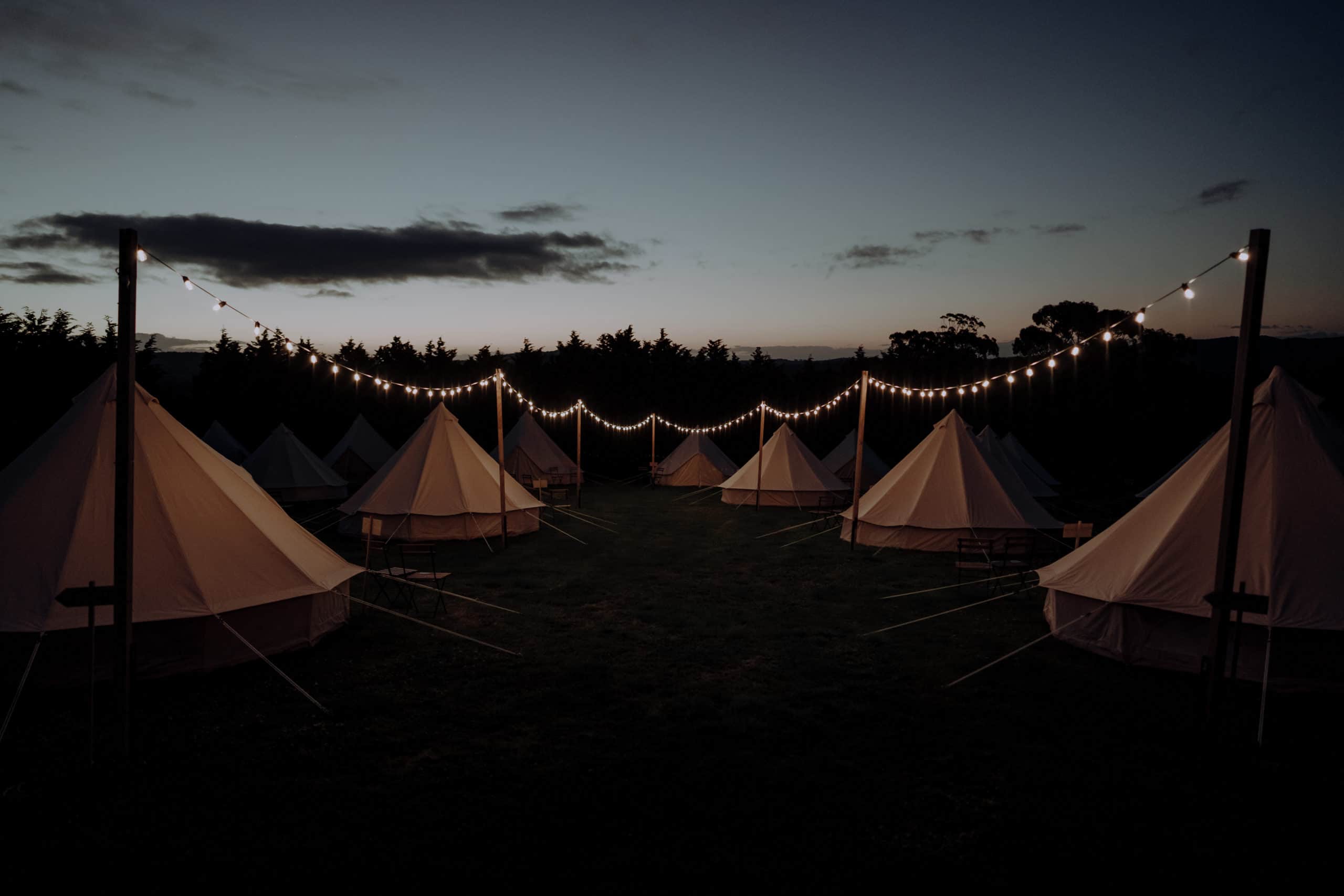 A glamping village featuring 20 bell tents at dusk with festoon lights 